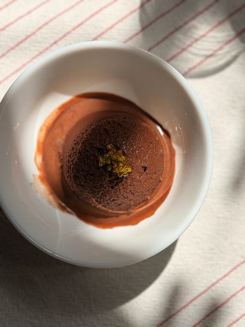 A dark chocolate sorbet dome in a white bowl, crowned with golden caviar pearls